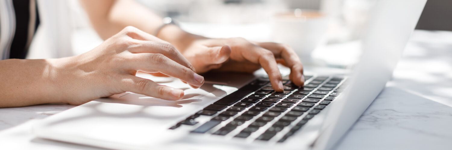 Hands of unrecognisable businesswoman typing on her laptop at cafe.