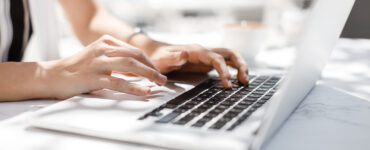 Hands of unrecognisable businesswoman typing on her laptop at cafe.