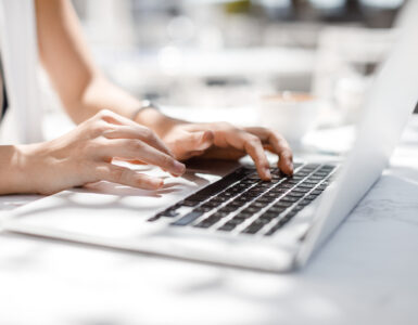 Hands of unrecognisable businesswoman typing on her laptop at cafe.