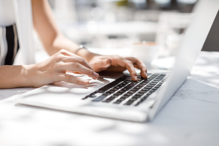 Hands of unrecognisable businesswoman typing on her laptop at cafe.